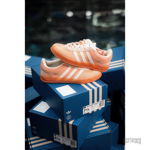 ADIDAS X BAD BUNNY GAZELLE INDOOR "CABO ROJO" sneakers in peach suede with white stripes, stacked on blue boxes.