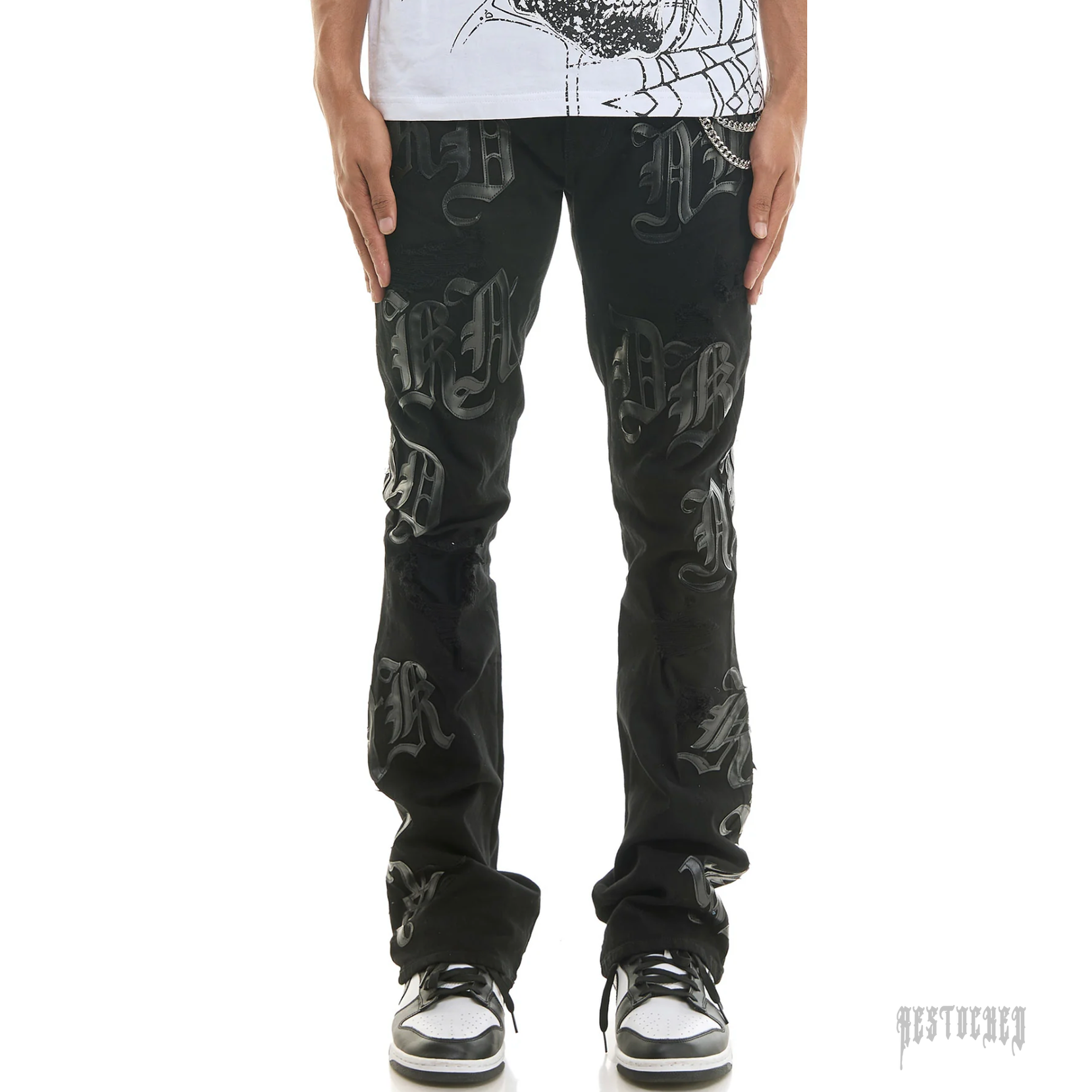 KDNK ONYX CIPHER KND4839 black distressed jeans with raised gothic lettering and a silver chain.
