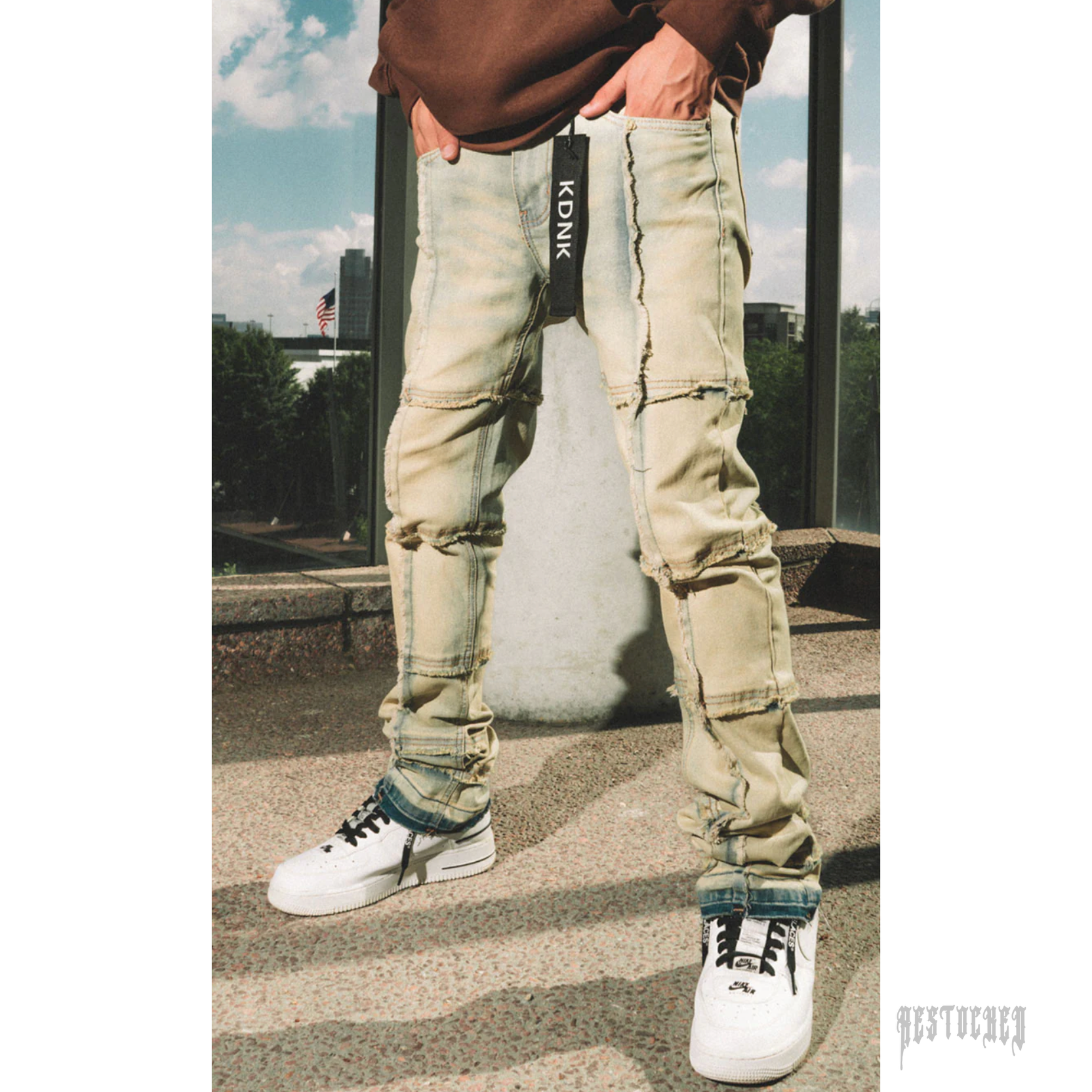 KDNK STACKED CUT light wash distressed denim jeans with stacked cuffs and black KDNK tag.