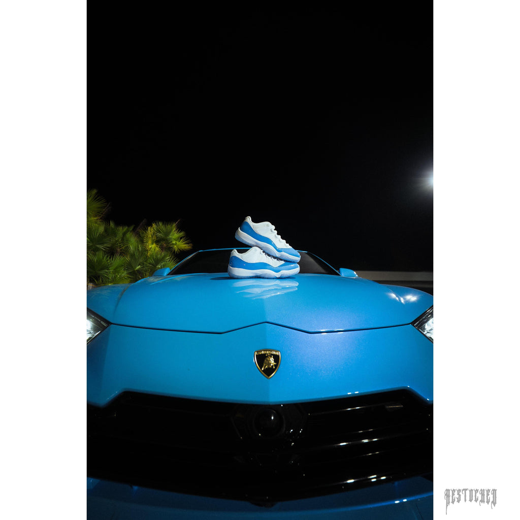 Jordan 11 Retro Low University Blue sneakers on a blue Lamborghini hood.
